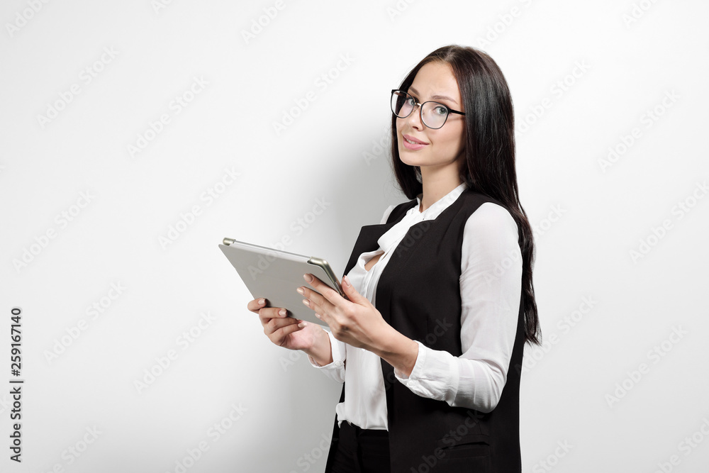 Portrait of a beautiful smiling woman blonde with a tablet in her hands in a business suit and jacket on a white background. A student or a businesswoman is working.