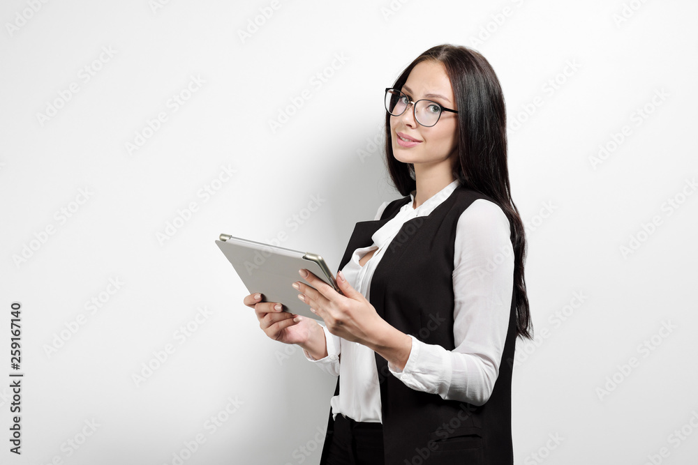 Portrait of a beautiful smiling woman blonde with a tablet in her hands in a business suit and jacket on a white background. A student or a businesswoman is working. Portrait of a beautiful smiling woman blonde with a tablet in her hands in a business suit and jacket on a white background. A student or a businesswoman is working.