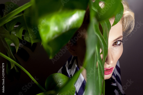 portrait of beautiful woman with green tropical leaves, closeup, indoor, studio shot on light grey background.