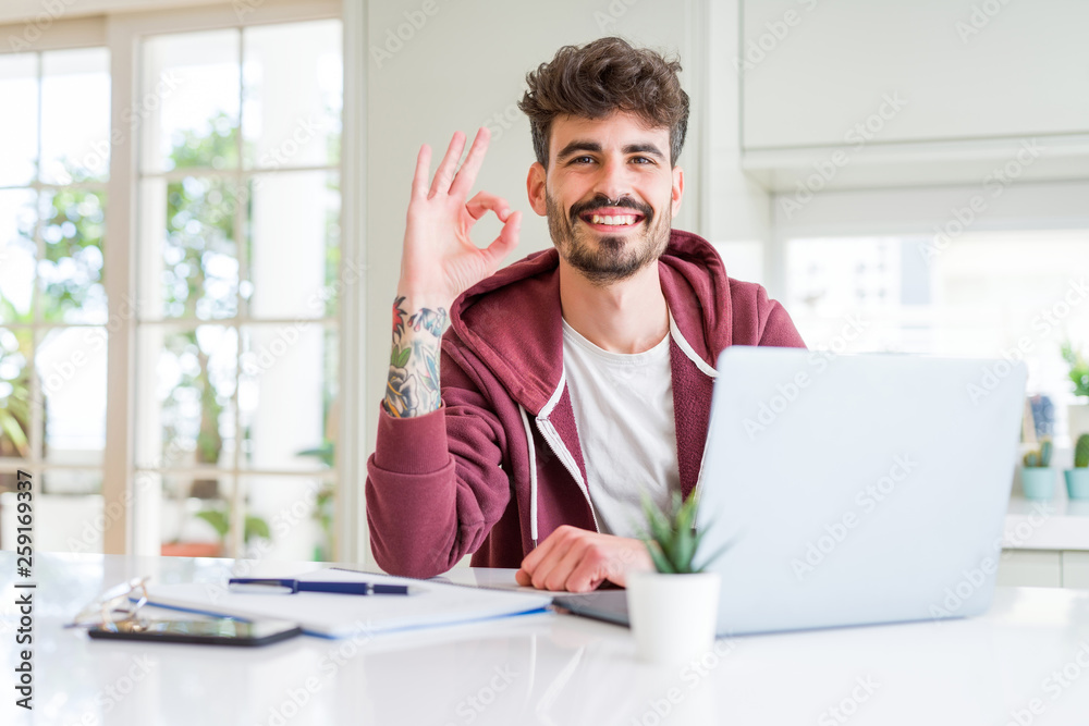 Young student man using computer laptop and notebook doing ok sign with fingers, excellent symbol Young student man using computer laptop and notebook doing ok sign with fingers, excellent symbol