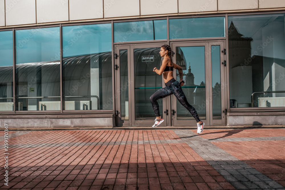 A woman runs in city in summer, a girl athlete runs, sportswear leggings top sneakers. Free space. The concept of a healthy lifestyle, motivation. Emotions of self-confidence, strength and speed.