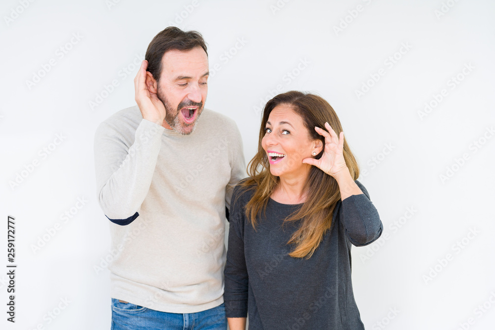 Beautiful middle age couple in love over isolated background smiling with hand over ear listening an hearing to rumor or gossip. Deafness concept. Beautiful middle age couple in love over isolated background smiling with hand over ear listening an hearing to rumor or gossip. Deafness concept.