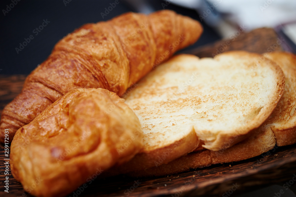 Toast and croissant on wooden plate