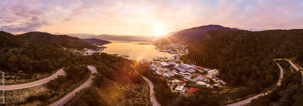 Sunrise over a mountainside covered in dense forest with a small harbour town at the bottom, Fethiye, Turkey panoramic