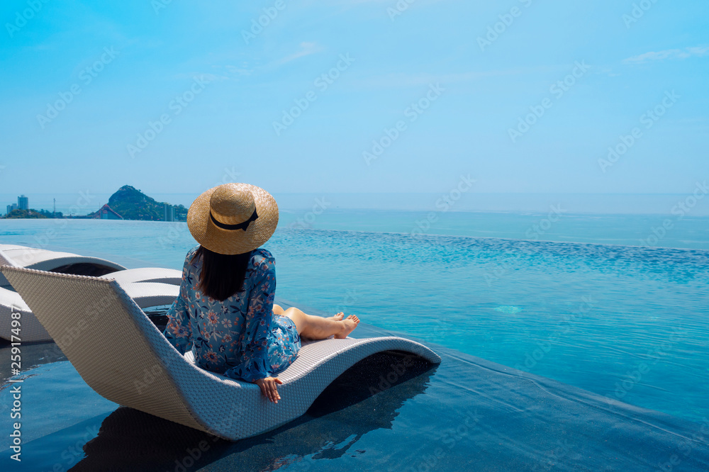 Tourist woman is sitting near the swimming pool side with great ocean view during summer vacation time.