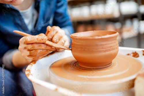 Woman making clay jug forming a shape with special tool on the pottery wheel, close-up view