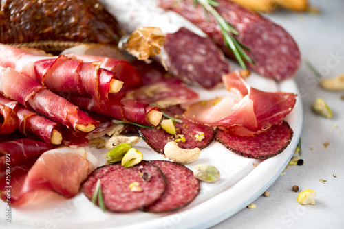 Cold smoked meat plate. Traditional italian antipasto, cutting board with salami, prosciutto, ham, pork chops, olives on grey background. Top view, copy space, flat lay