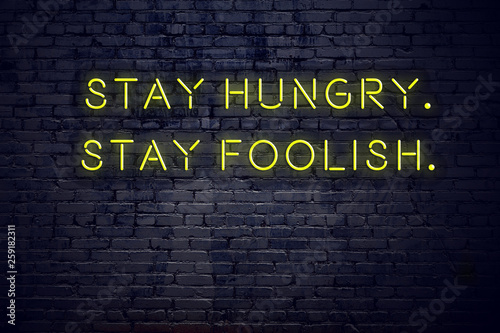 Positive inspiring quote on neon sign against brick wall stay hungry stay foolish