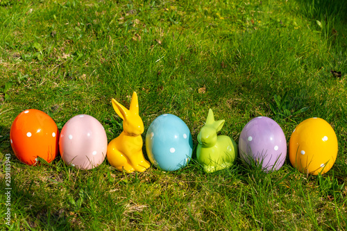 Canvas Print Colorful ceramic easter eggs and Easter bunnies in a line on a meadow
