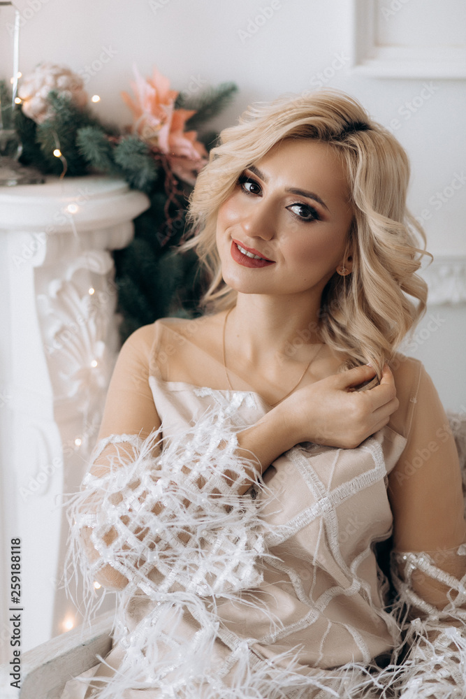 Charming blonde woman in white dress poses in a room with large Christmas tree Charming blonde woman in white dress poses in a room with large Christmas tree