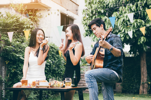 Women enjoying drinks party with guy playing guitar singing at home garden outdoors.