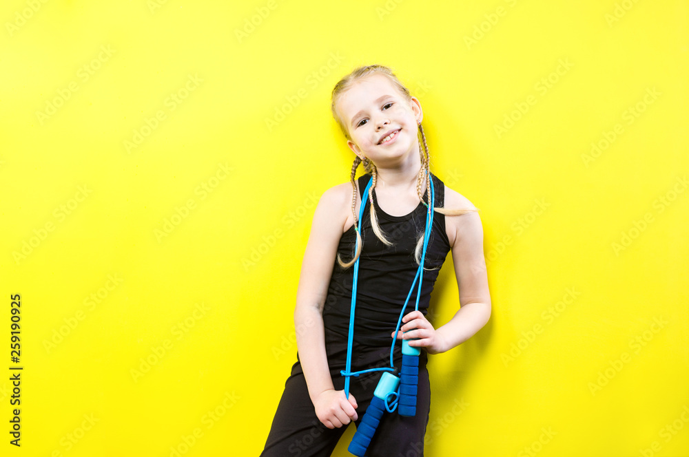 Theme sport and health. Beautiful caucasian child girl with pigtails posing yellow background with smile. little athlete holds sport rope in hands. Banner advertising, space for text copy space blank