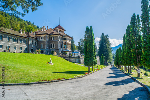 Cantacuzino castle entrance with green lawn and front road with thuja trees on each side. Built in Neo-Romanian style. Located in Busteni, Romania, Eastern Europe.