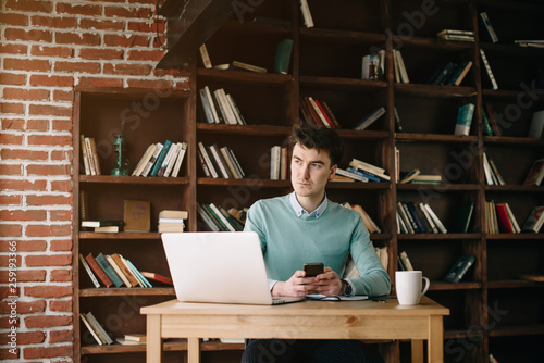 Young handsome student typing on his notebook his diploma. Student discussing on the phone universities's timetable. Education online. Work on freelance. Software development.