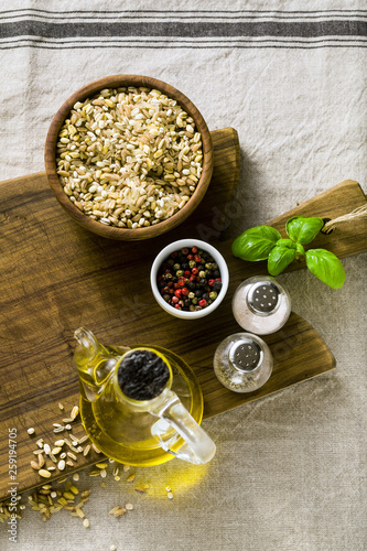 mix of cereals in a wooden bowl on a cutting board with olive oil, multicolored peppers and spices. food background home cooking on linen tablecloth