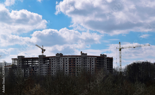 Crane - machine designed to lift and move in the cargo space, trawl, at the construction site against a blue sky with white clouds