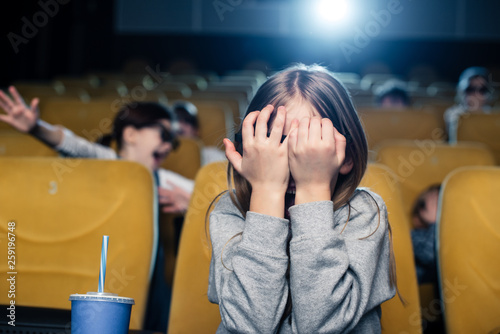 frightened child holding hands on face while watching movie in cinema