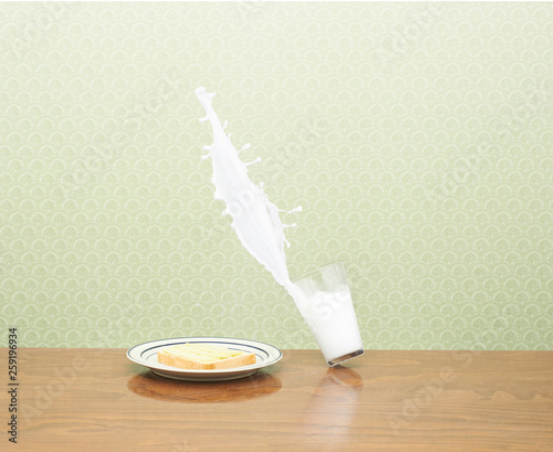 Milk spilling from glass besides breakfast plate on wooden table