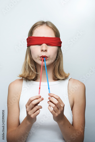 Young blindfold woman holding straw in mouth against gray background