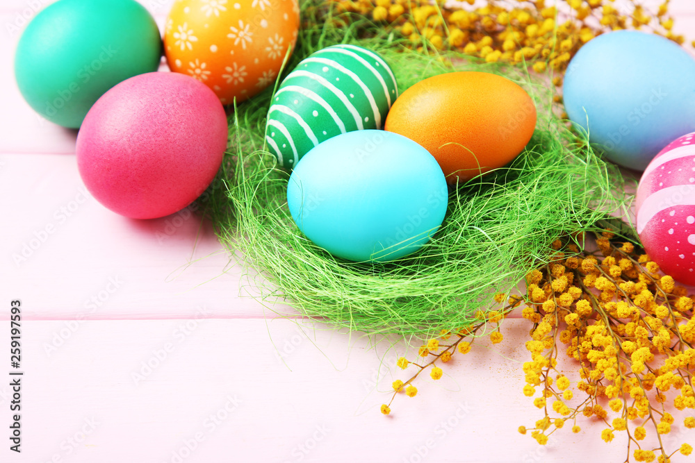 Colorful easter eggs in nest with yellow flowers on wooden table