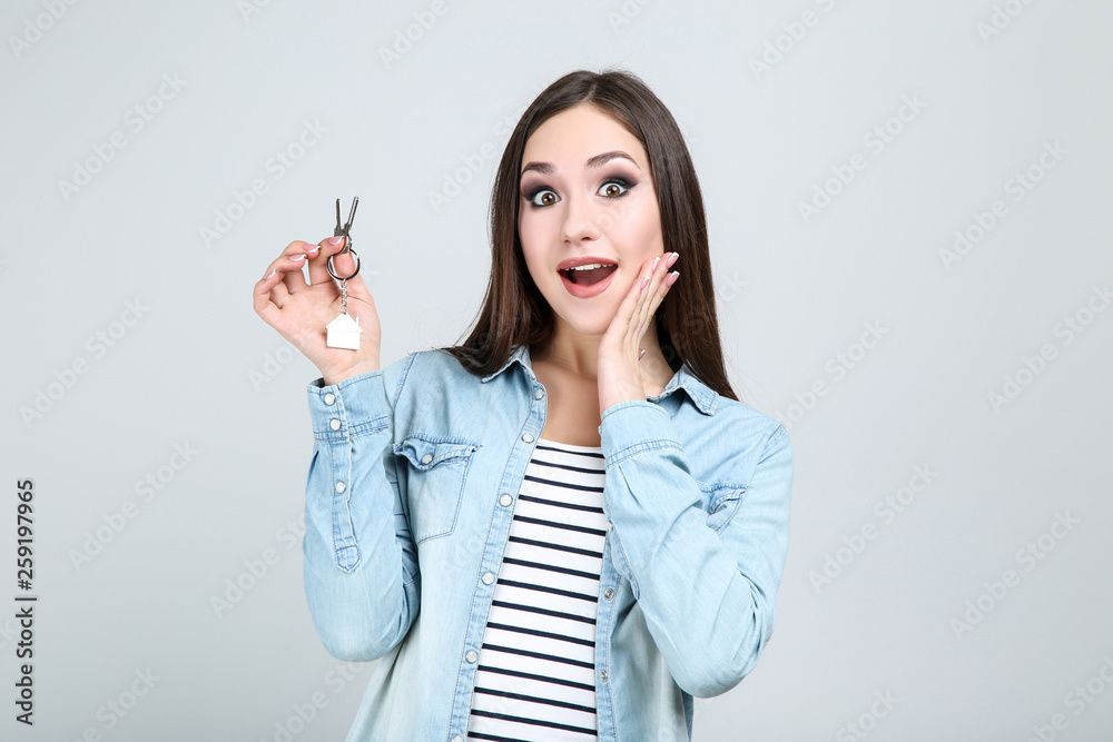 Young woman showing house keys on grey background Young woman showing house keys on grey background