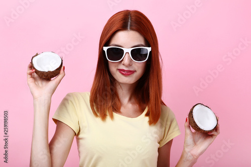 Young redhaired woman with coconuts on pink background