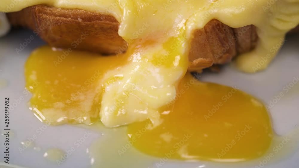 Soft yolk of a poached egg dripping down on eggs benedict. American breakfast or brunch dish. Soft yolk of a poached egg dripping down on eggs benedict. American breakfast or brunch dish.