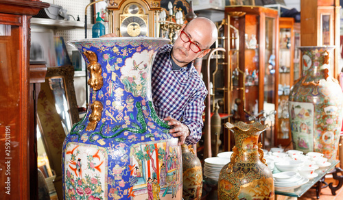 Experienced appraiser of antiques shop measuring antique vase while determining value photo