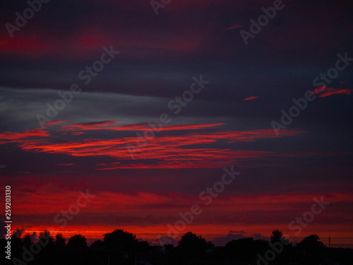 Dramatic sunset sky over small town silhouette. Rich red and blue tones.