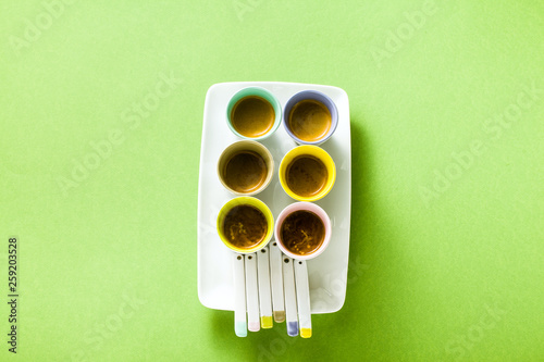Six multicolored cups of Italian espresso coffee with porcelain spoons on a serving plate. on a green background.
