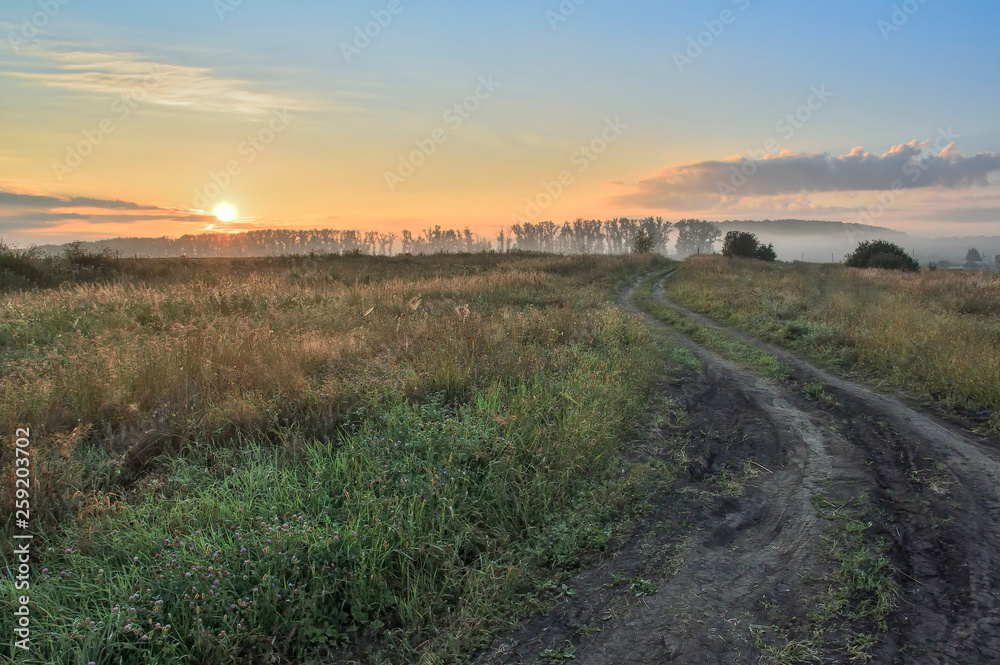 morning, rising sun over the field and dirt road, with trees and country buildings