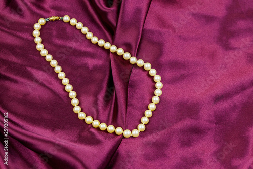 Pearl necklace on purple satin fabric background