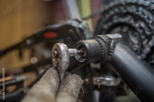 A close-up of a male bicycle mechanic's hand in the workshop uses a screwdriver tool to adjust and repair the bicycle crank assembly, the front bike stars