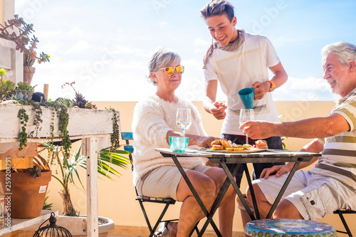 grandfathers adult mature and teenager nephew enjoy outdoor in the terrace some leisure with food and drinks. ocean and city view, vacation sunny day nice weather concept and background. happy people