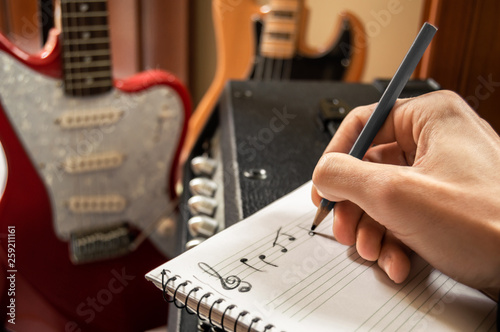 Canvas Print Young man composing music in a staff notebook with guitar and bass in the background