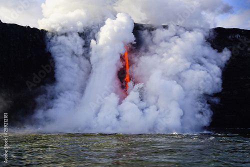 Hot lava flows from high cliff into the ocean in Big Island in Hawaii