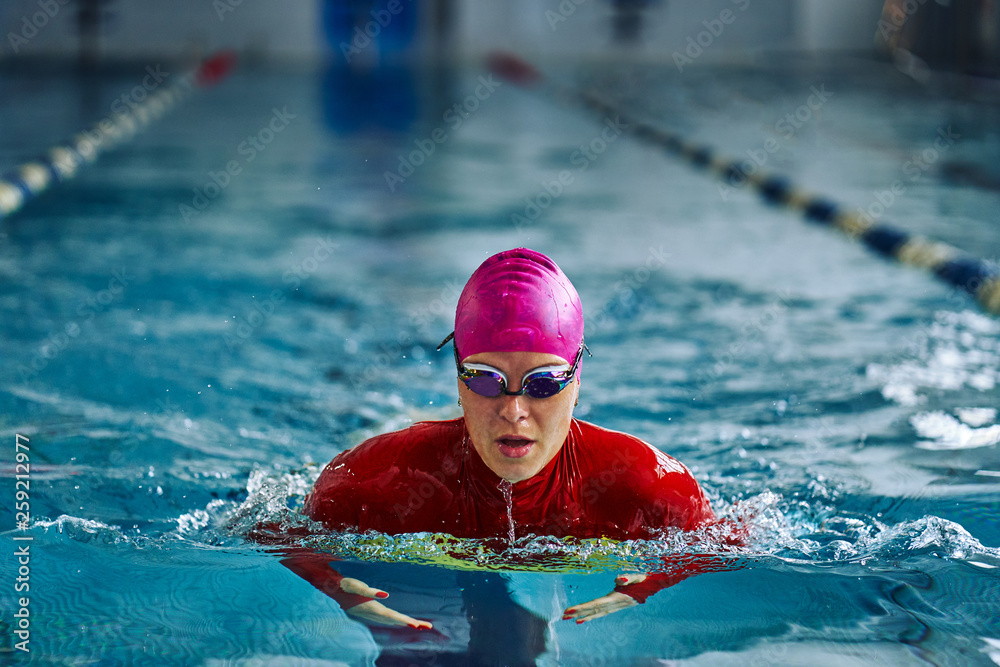 Female athlete in a red-yellow swimsuit is swimming in the style of breaststroke. Splashes of water scatter in different directions.