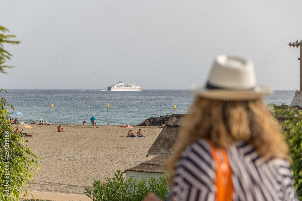 View of a beach with tourists, observed by a woman walking nearby