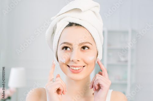 happy young girl with a towel on her head apply a cleansing mask on her face