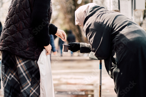 Photo of passerby givining alms for old hungry homeless female beggar on street photo