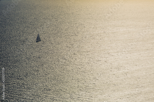 Seascape with small sailing boat with stretched sails. Beautiful sunset, sun reflecting in sea waves, boat in sunlit. Creative view from above. © Martin