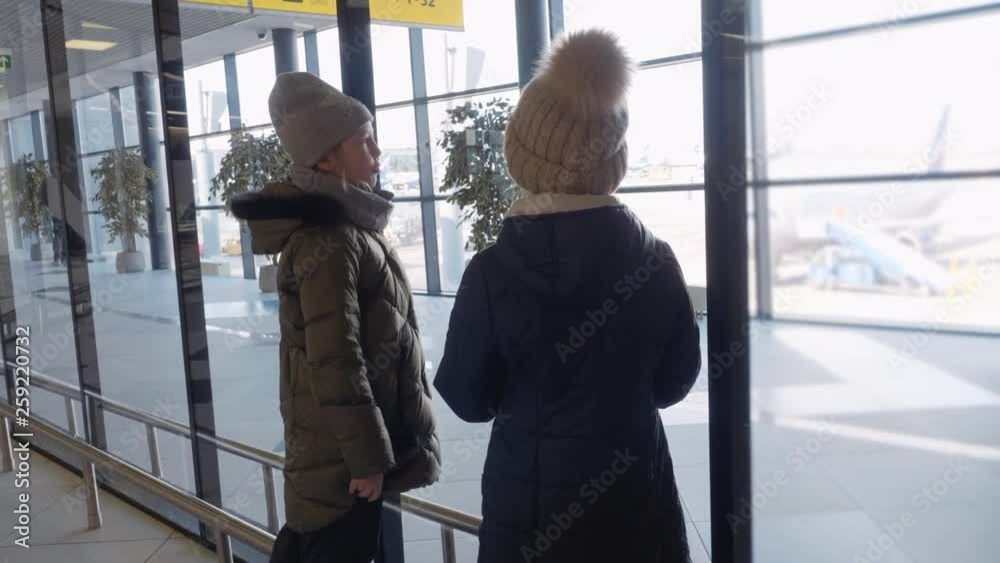 Girls teenager looking to airport window while waiting aircraft in departure lounge. Young girl looking to airplane from airport window on waiting area Girls teenager looking to airport window while waiting aircraft in departure lounge. Young girl looking to airplane from airport window on waiting area