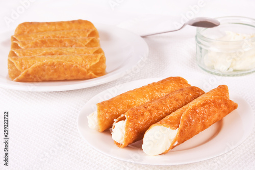 Cream filled brandy snaps served on a plate. Unfilled snaps and a pot with cream in the background