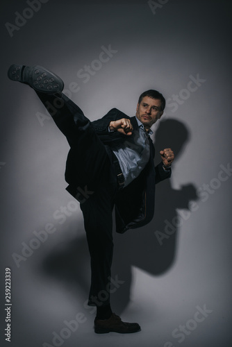 a man, business man in black suit is kicking on black background