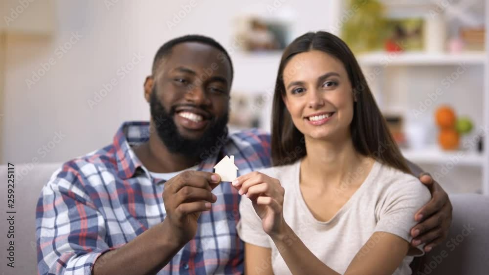 Hugging mixed-race couple holding paper house, real estate purchase, mortgage