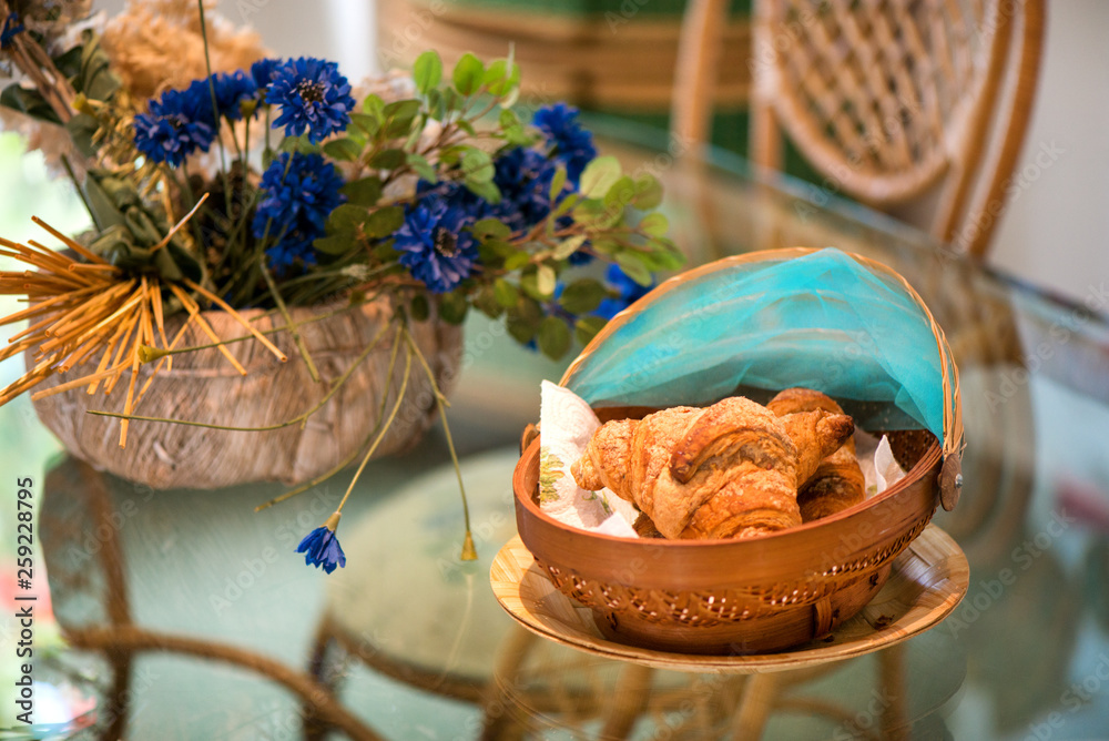 Freshly baked croissants in a woven basket put on a modern glass table in a large kitchen
