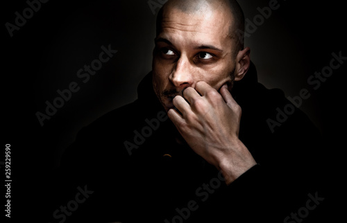 Dramatic dark portrait with strong contrast and film grain of young man sitting in the room with sadness and depression in his eyes thinking about life