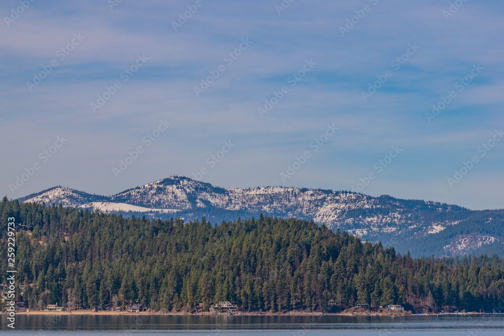 Snow capped mountains with evergreen trees and lake in spring