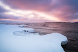 snow on rocks at the coast and sunset in the background