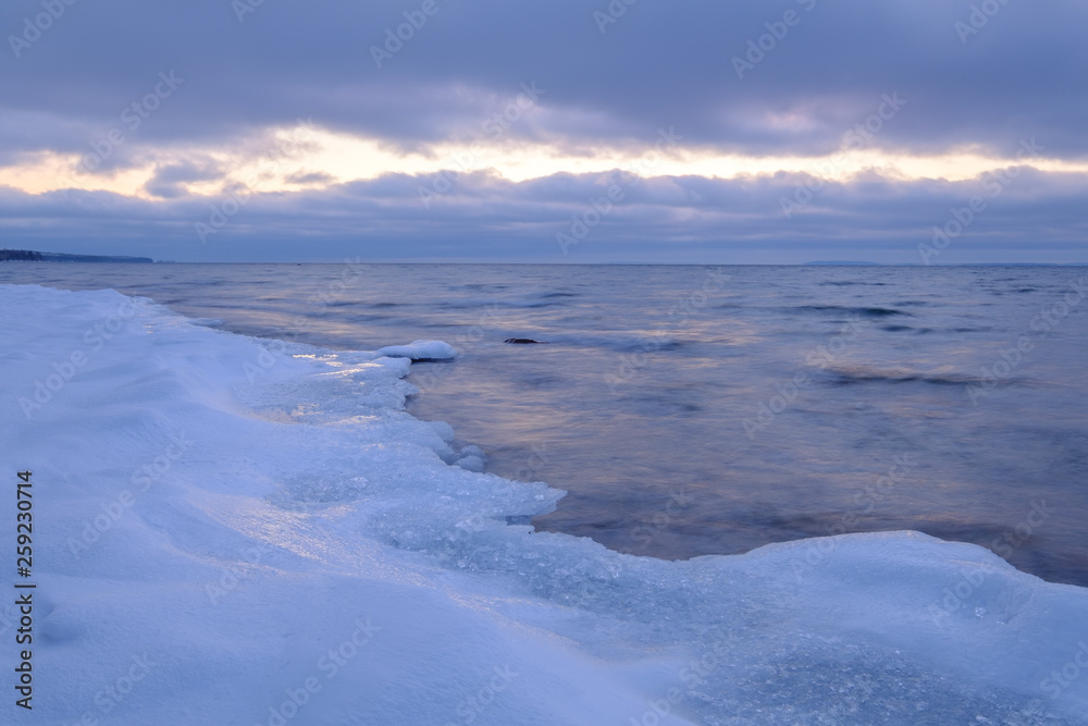 ice and snow on a beach in the foreground, clouds and a streak of light in the background